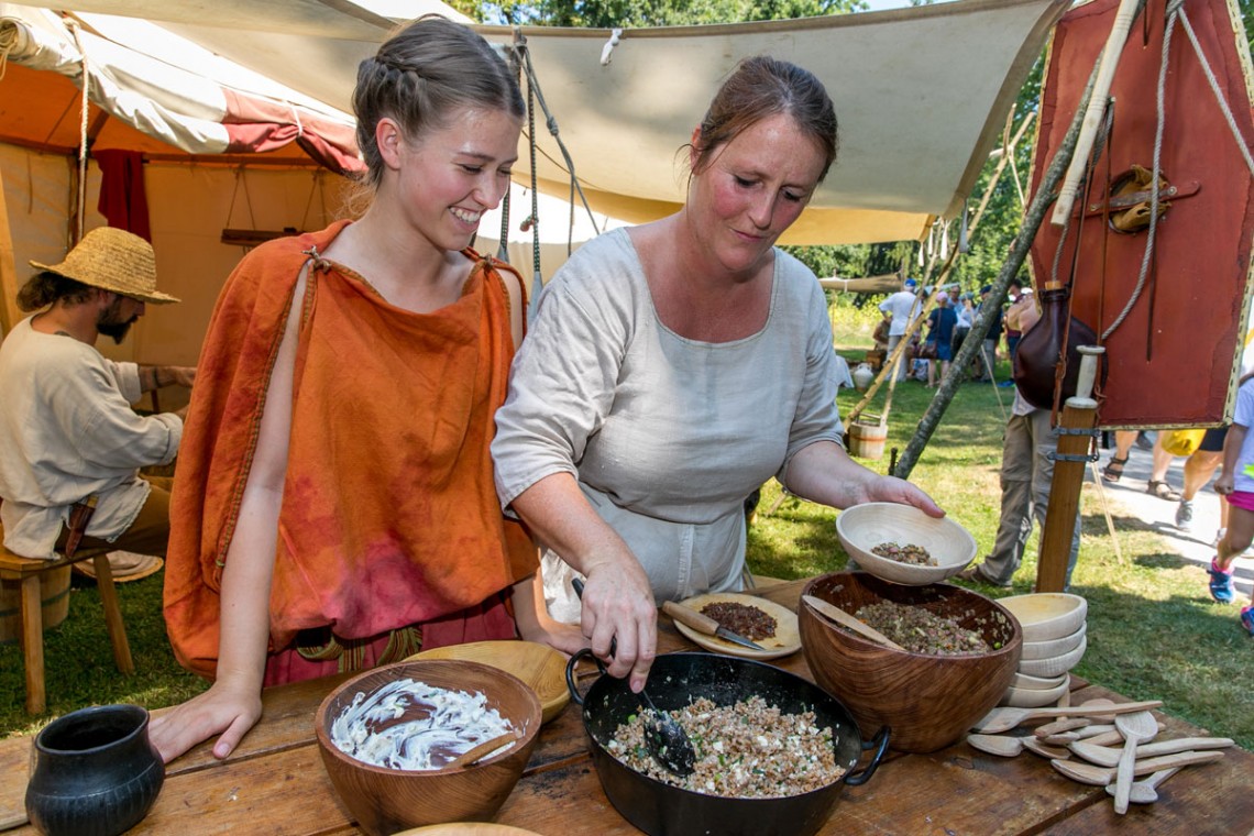 Schauzelt &quot;Römische Küche&quot;: Zwei Frauen in römischen Gewändern bereiten Essen in unterschiedlichen Holzschüsseln zu