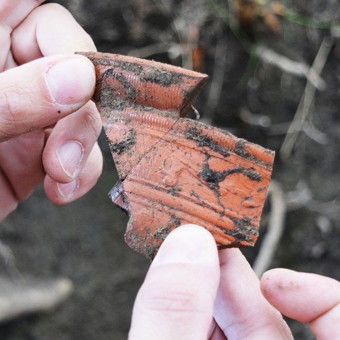 Hände halten zwei Scherbenstücke voller Erde
