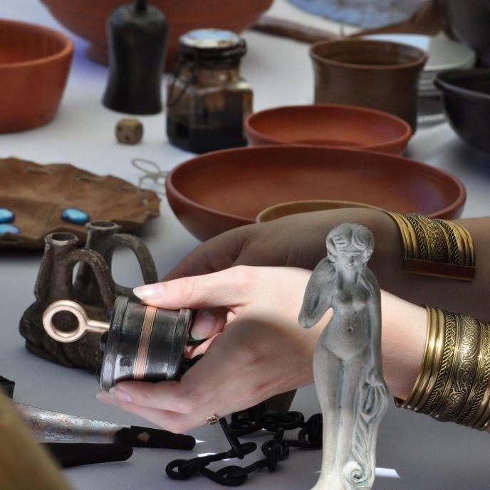 Tisch mit unterschiedlichen Nachbildungen römischer Gegenstände, Hände befühlen Schloss