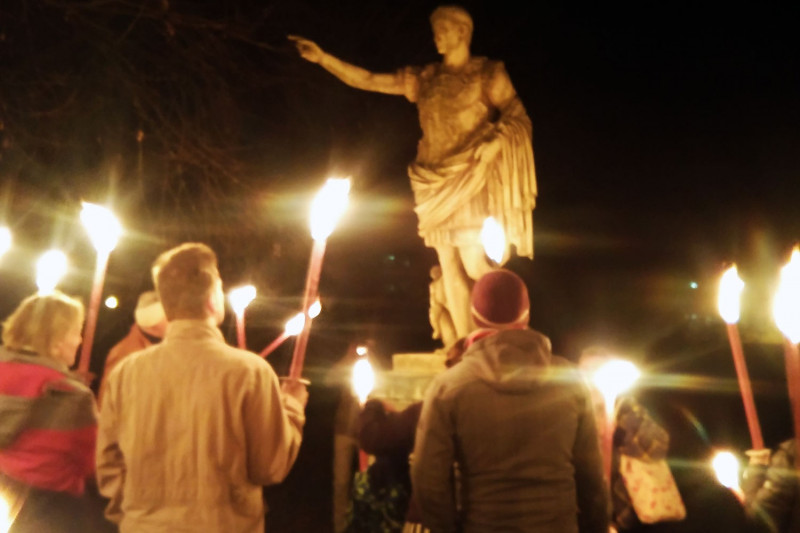 Menschengruppe mit Fackeln bei Nacht vor Augustusstatue